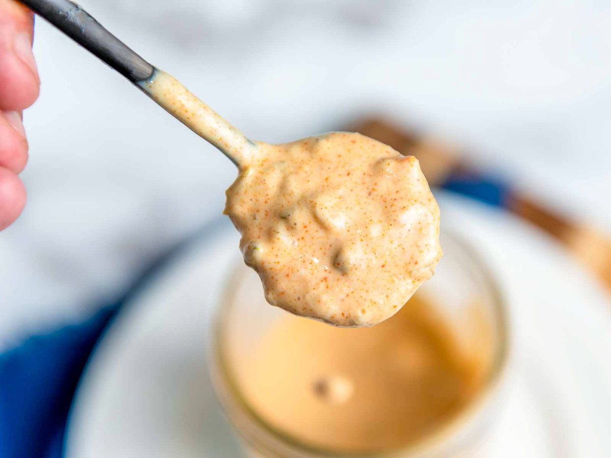 Close-up of a spoonful of creamy homemade Big Mac copycat sauce with visible relish and seasoning, held above a mason jar.