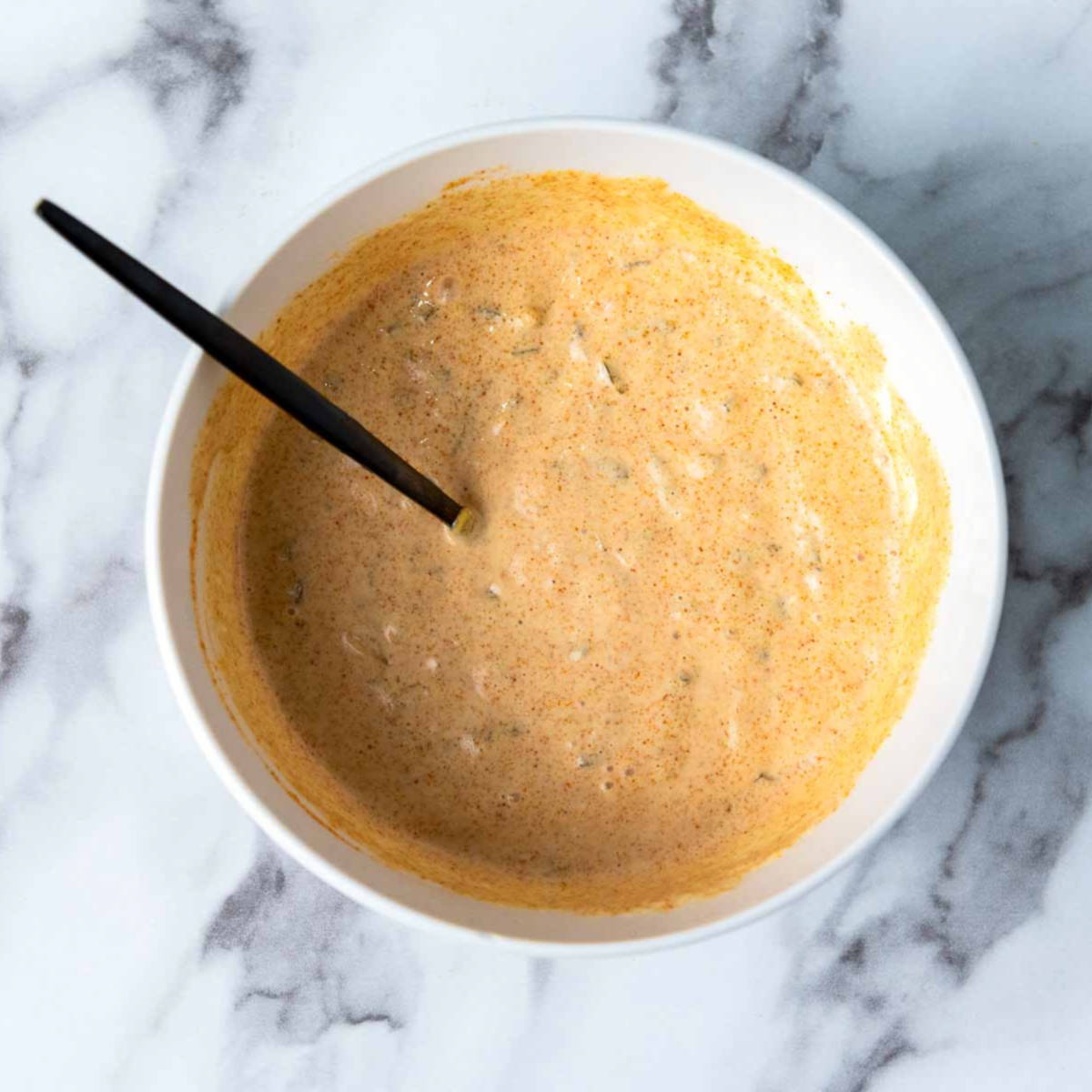 Ingredients of big mac sauce mixed in a white bowl and placed on a marble surface.