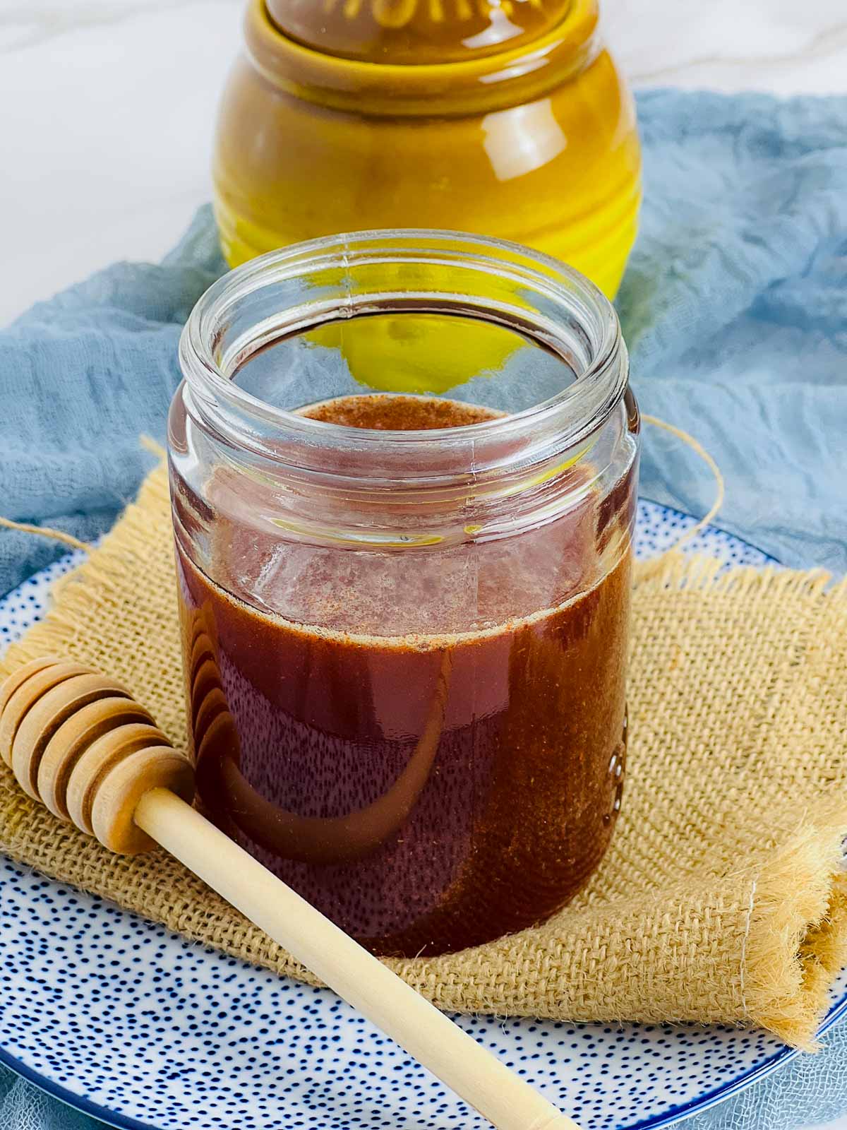 A jar of hot honey with a honey stick placed beside it.