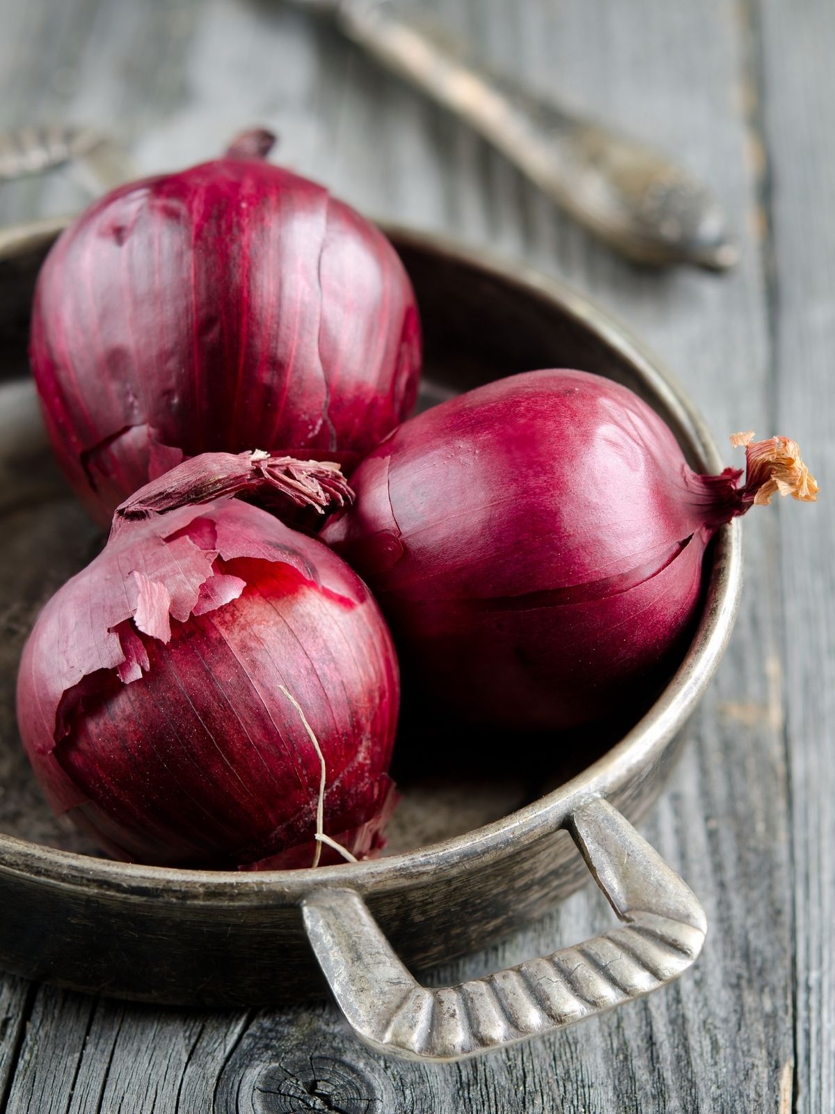 Three red onions placed in a bowl on a wooden surface.