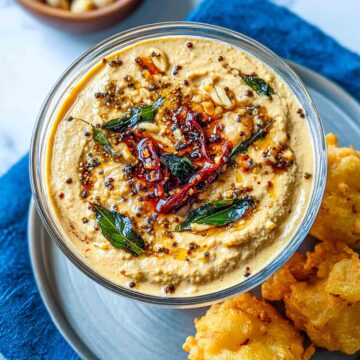 Close-up of smooth peanut chutney with a spiced oil tempering of mustard seeds, curry leaves, garlic, and red chilies in a glass bowl.