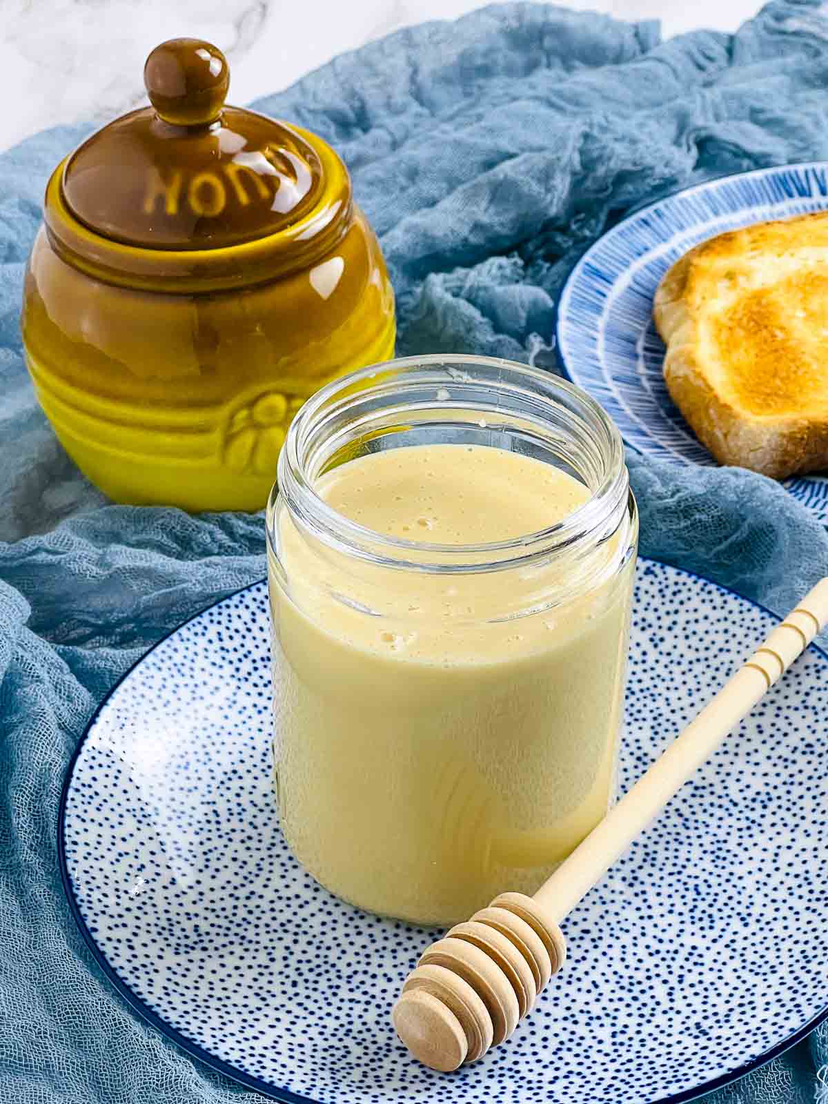 A jar of whipped honey with a honey stick placed on the side.