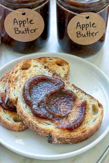 Toast topped with apple butter with jars of apple butter in the background.