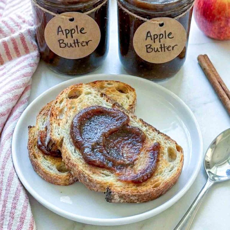 Toast topped with apple butter with jars of apple butter in the background.