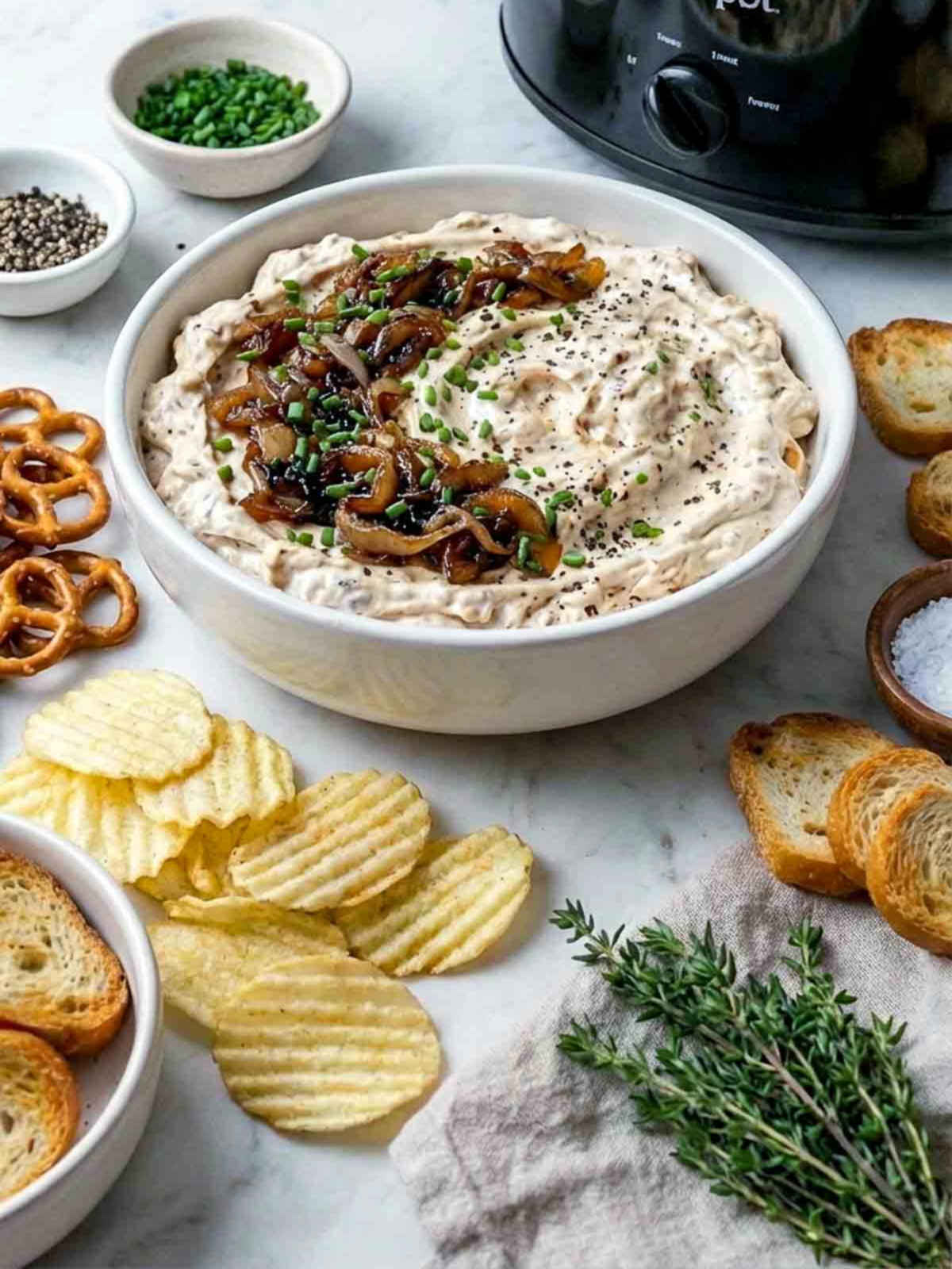 Creamy caramelized onion dip topped with sautéed onions and chives, served with chips, pretzels, and toasted bread.
