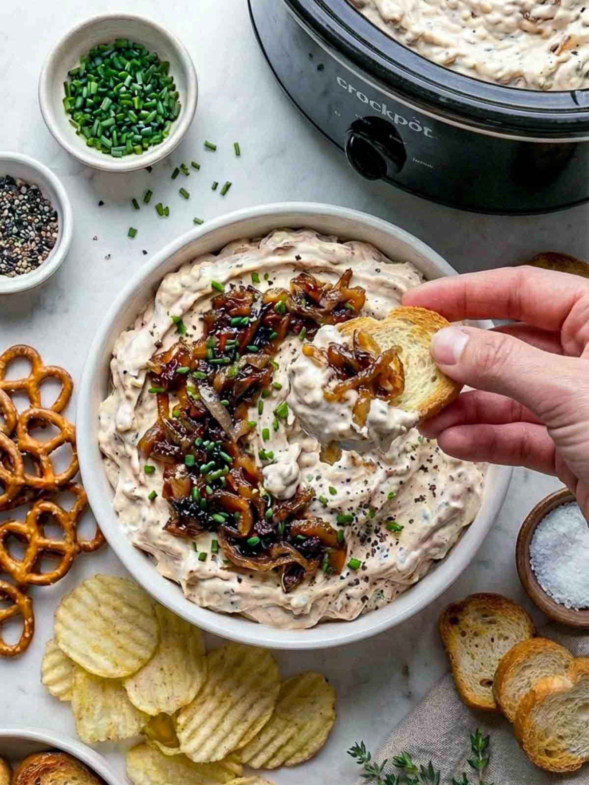 Woman scooping onion dip using a chip from the serving bowl.