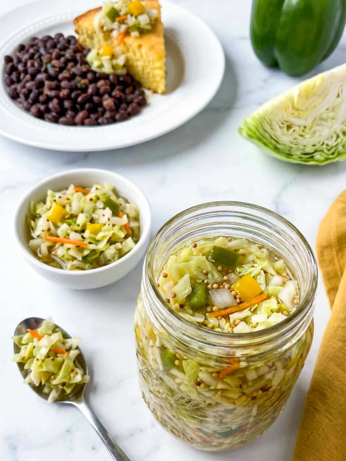 Jar of chow chow relish with cabbage, peppers, and carrots beside beans and cornbread.