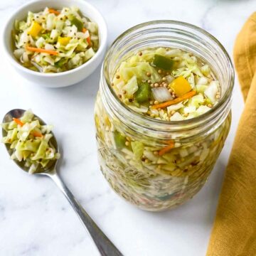 Jar of chow chow relish with cabbage, peppers, and carrots beside a spoon and small bowl.