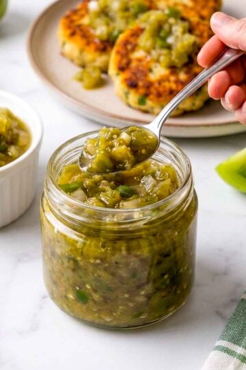Woman holding a spoonful of green tomato relish over the jar.