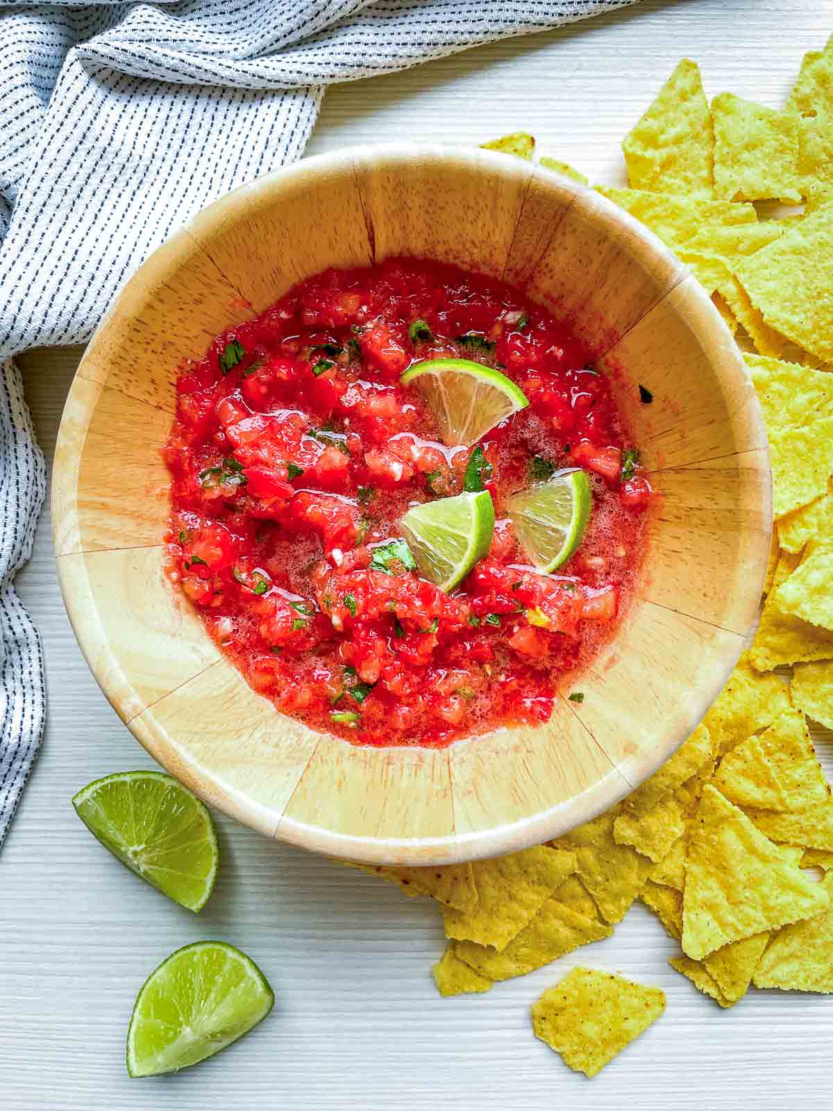 Bowl of fresh tomato salsa with lime wedges and tortilla chips.