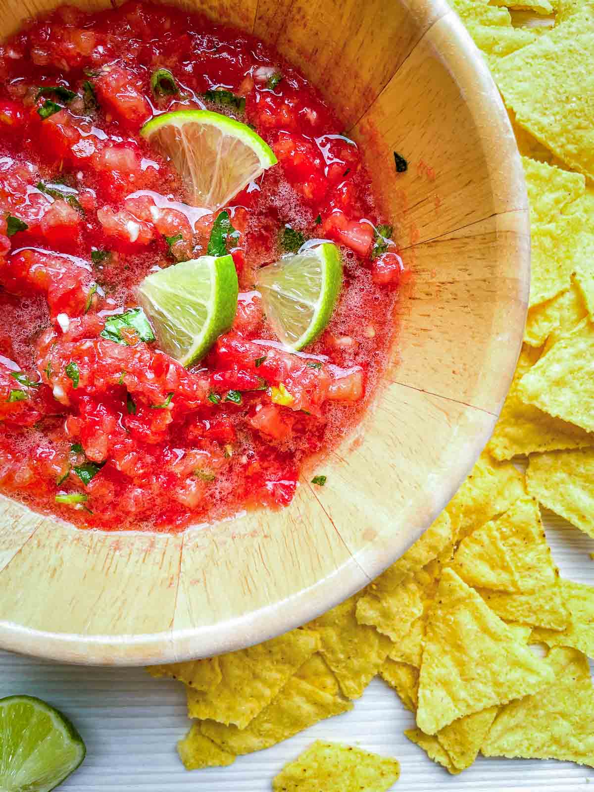 Close-up of fresh tomato salsa with lime wedges and tortilla chips.