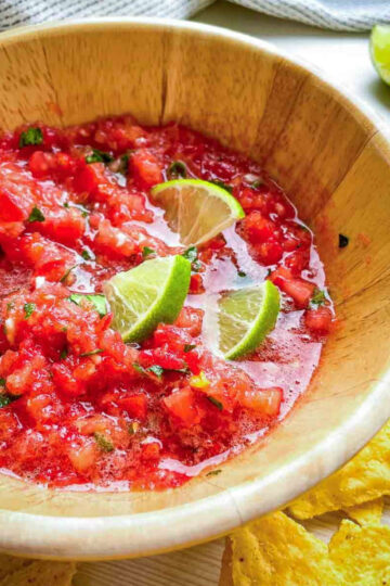 Bowl of fresh tomato salsa with lime wedges and tortilla chips on the
