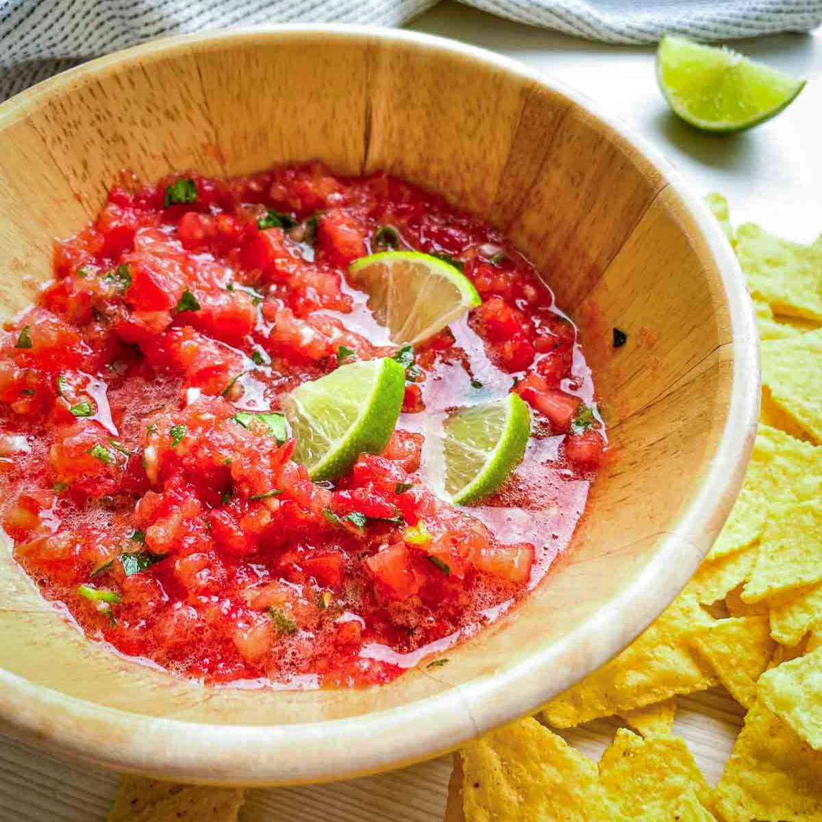 Bowl of fresh tomato salsa with lime wedges and tortilla chips on the