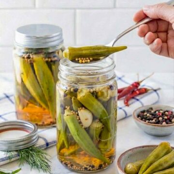 Close up of a hand holding pickled okra using a spoon over the jar.