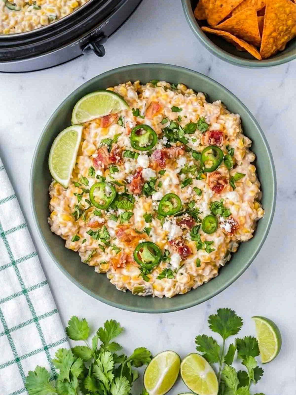 Roasted corn jalapeño street corn dip topped with cilantro, jalapeño slices, and lime wedges.