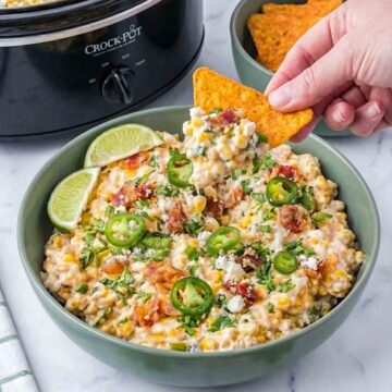 Hand dipping tortilla chip into roasted corn jalapeño street corn dip.