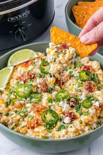 Hand dipping tortilla chip into roasted corn jalapeño street corn dip.