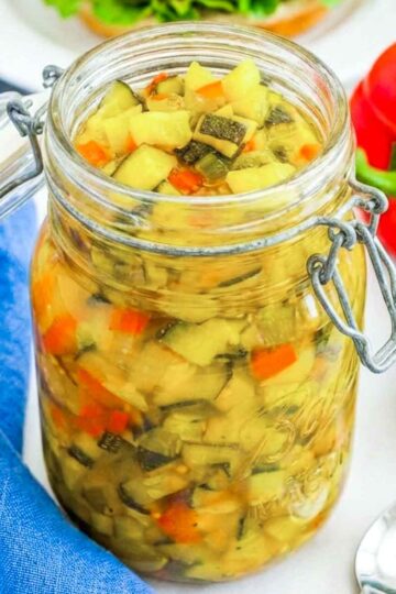 Glass jar filled with homemade zucchini relish made with diced zucchini, peppers, and spices in a golden brine.