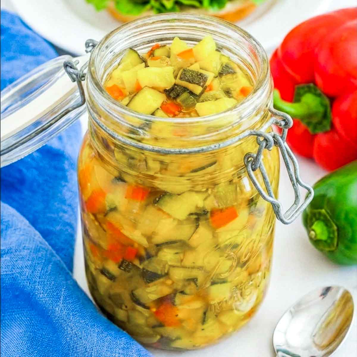 Glass jar filled with homemade zucchini relish made with diced zucchini, peppers, and spices in a golden brine.