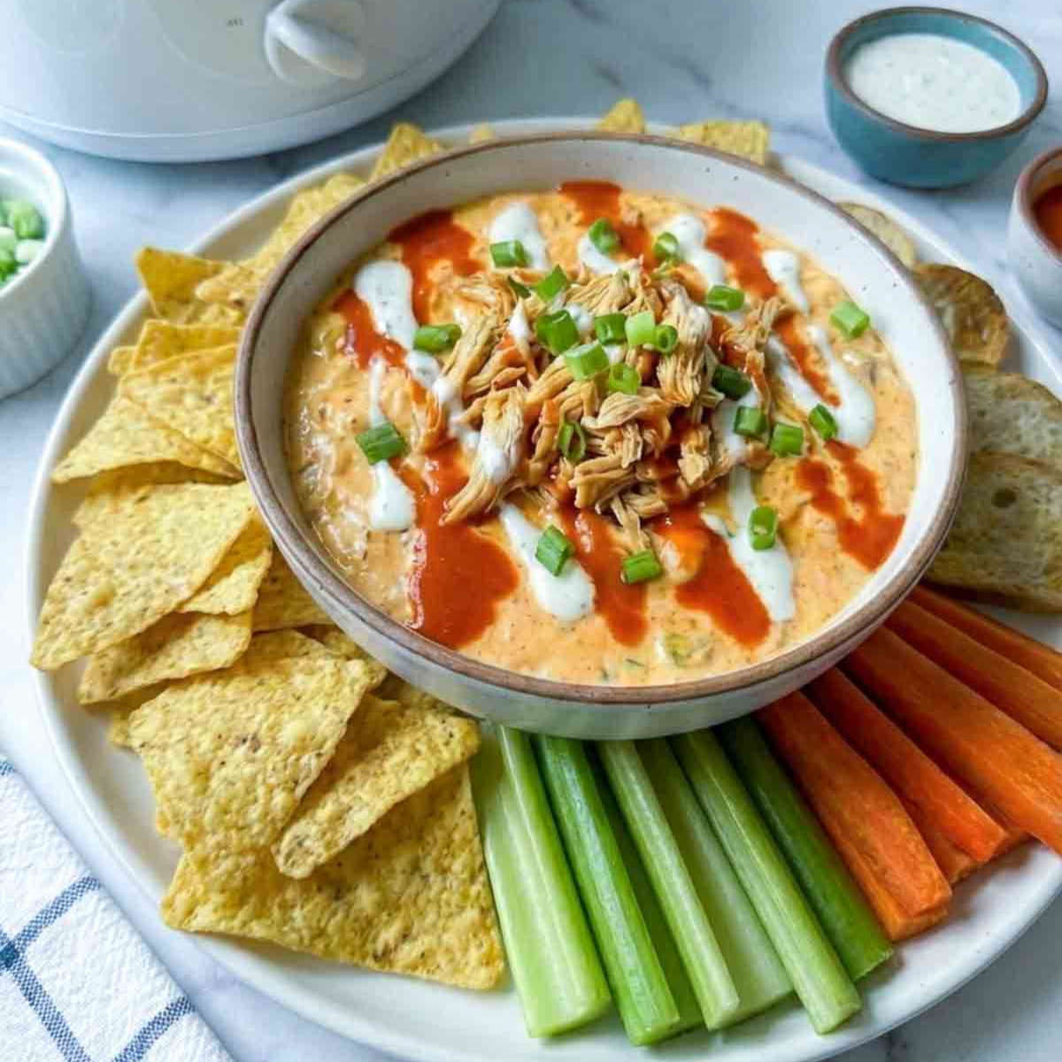 Side view of crockpot buffalo chicken dip served with dippers.