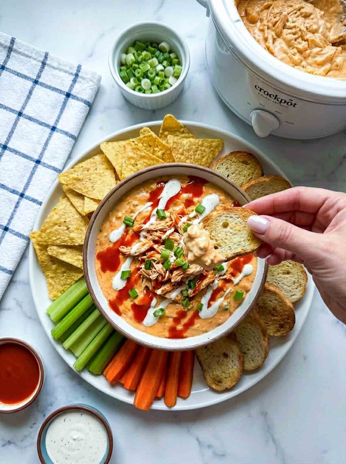 Woman scooping crockpot buffalo chicken dip and holding it above the bowl.