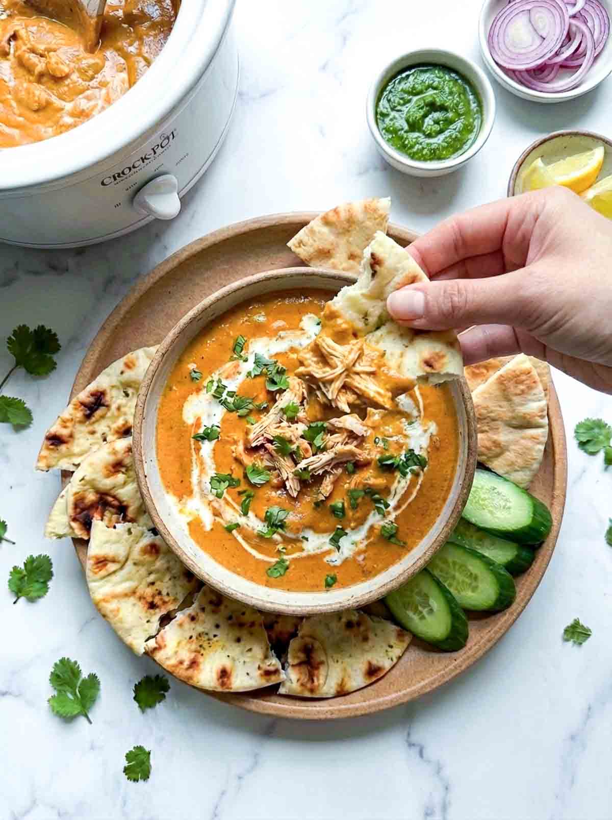 A person dipping a piece of naan into the butter chicken dip.
