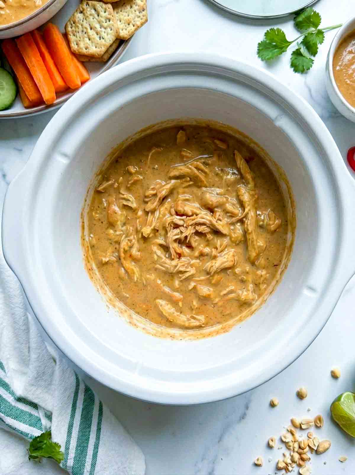 Peanut chicken dip in a crockpot placed on a white marble surface.