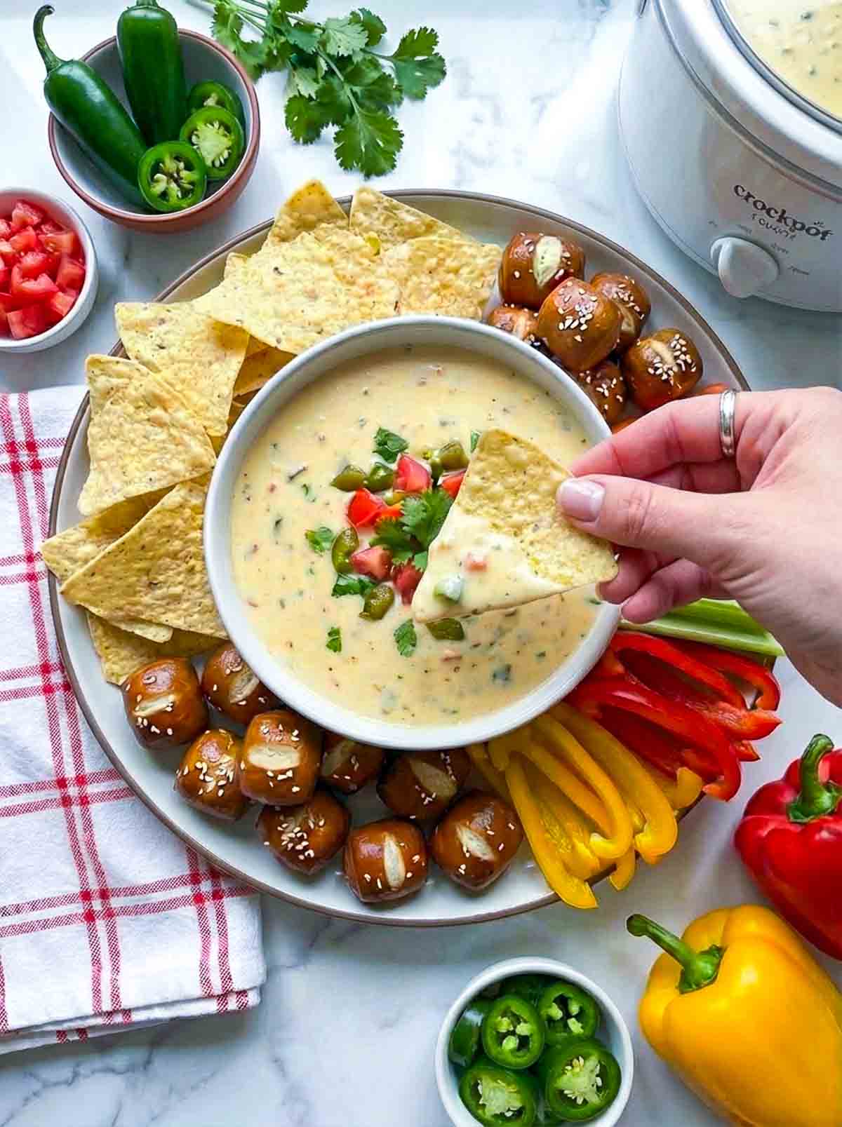 Person dipping a tortilla chip in the cheesy queso dip.