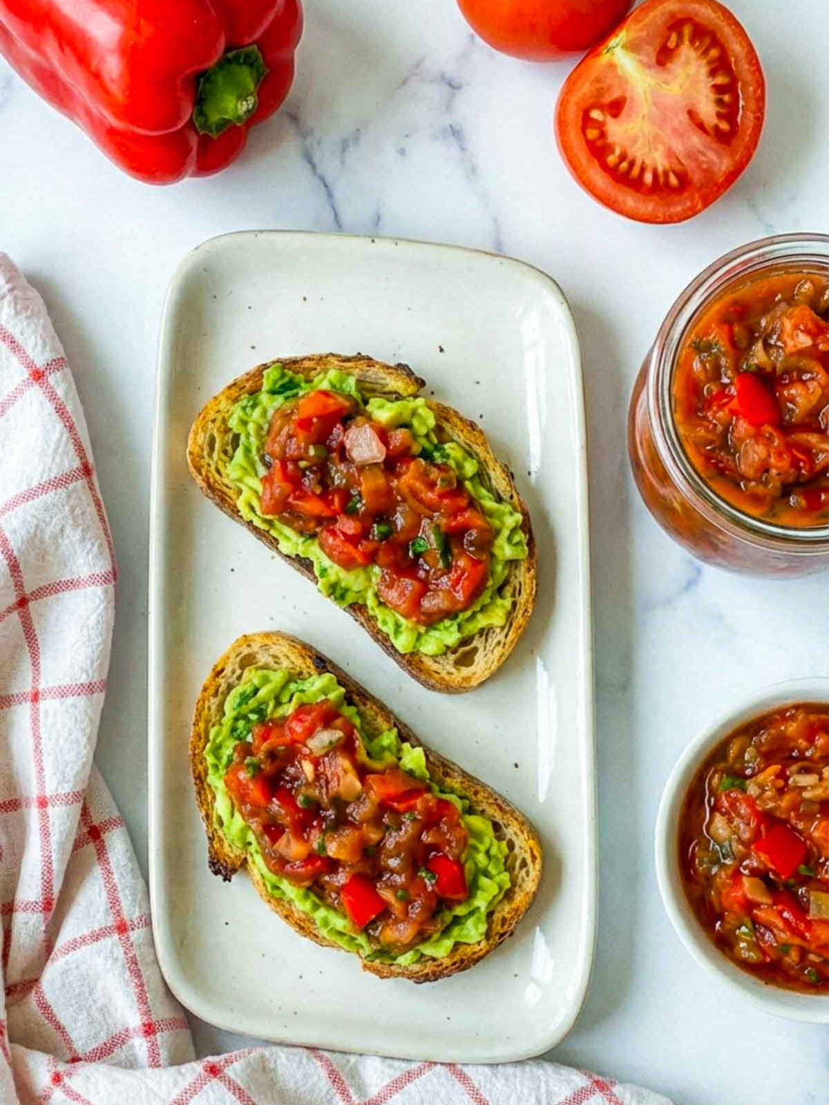 Top view of avocado toast topped with tomato relish placed on a white plate.