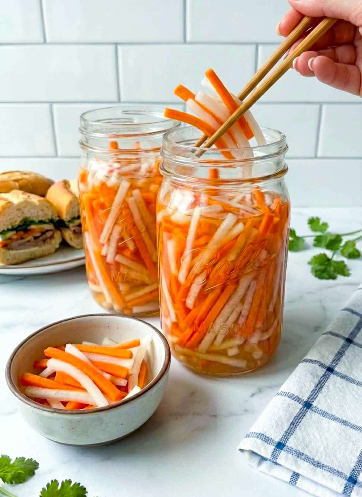 Persone pickling some Vietnamese pickled carrots and daikon using chopsticks from a jar.