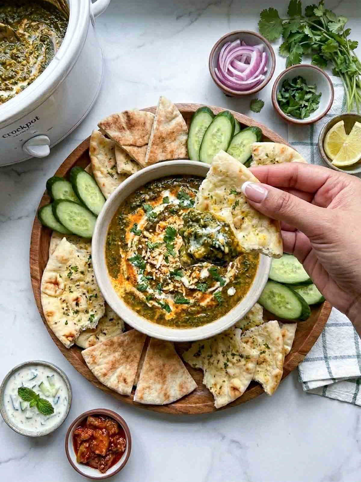 A woman scooping out saag paneer dip using a piece of naan.