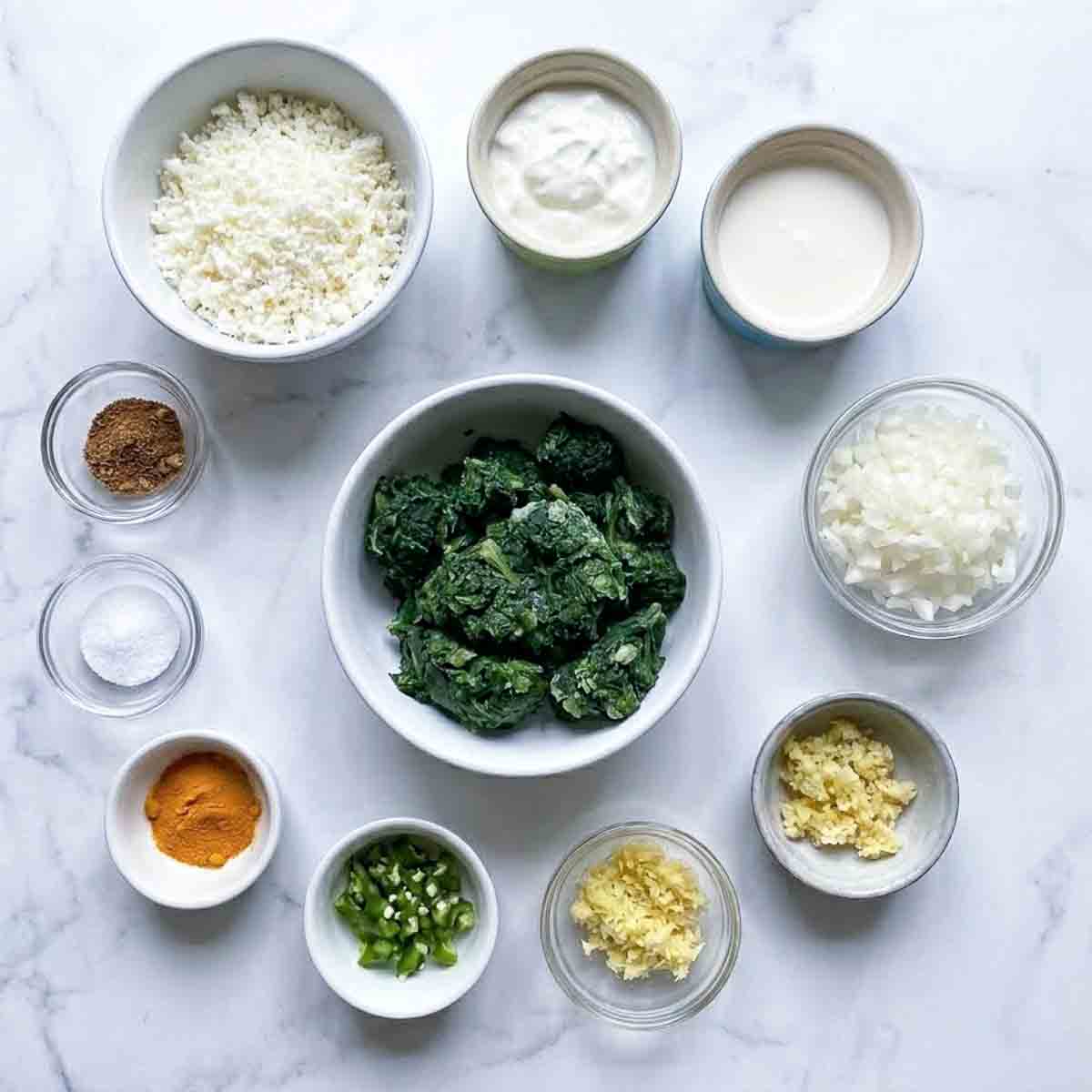 Ingredients to make saag paneer dip placed on a white marble surface.